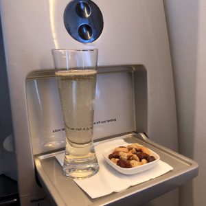 a glass of liquid and a bowl of nuts on a tray